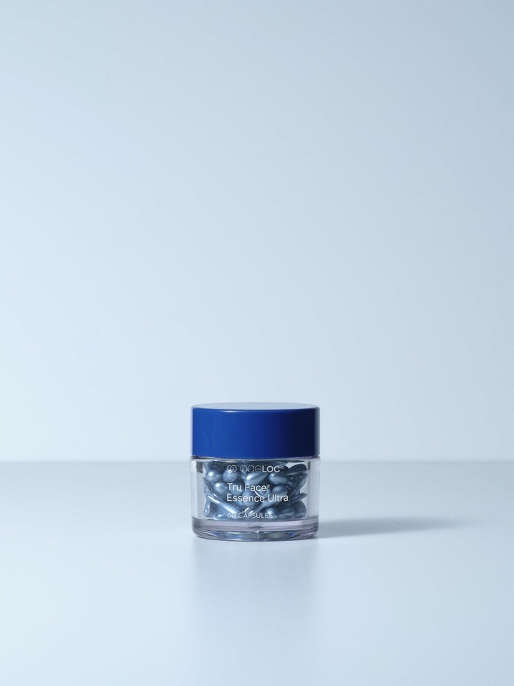 A clear glass jar with a navy blue lid contains silver-colored tru face essence capsules labeled ageloc tru face essence ultra