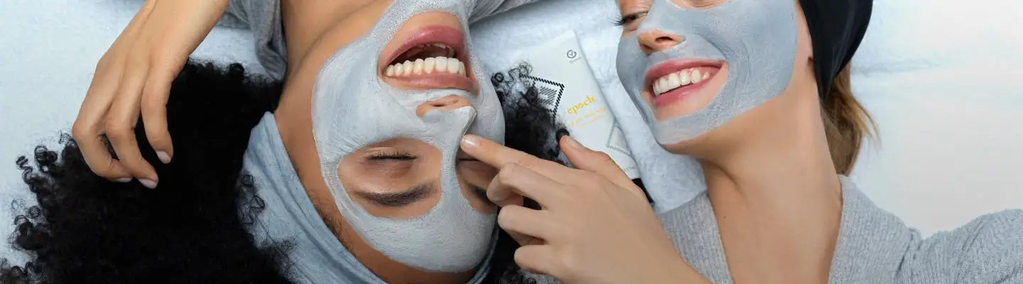 Graue Gesichtsmaske auf beiden Gesichtern aufgetragen, wobei eine Person ein weißes Paket mit schwarzer und gelber Markenbeschriftung in der Hand hält.